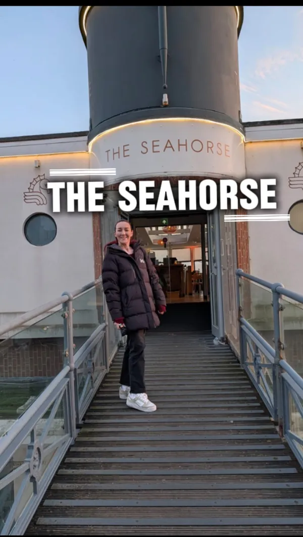 The video promotes a bottomless dinner offer at 'The Seahorse' restaurant in Brighton. It showcases the restaurant's exterior, interior decor, and scenic sunset views over the beach. A variety of drinks are featured, including prosecco, cocktails like Aperol Spritz and Espresso Martini, and rosé wine. The food shown includes nibbles like olives, popcorn, and focaccia with pesto. The main courses highlighted are a pan-roasted chicken breast with stuffing and maple carrots, and a Sri Lankan sweet potato curry with rice and flatbread.