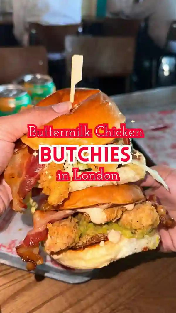 The video showcases a meal from Butchies, a fried chicken restaurant in London.  It features two burgers (Jenny from the Block and BBQ B-Boy), skin-on fries, chili honey, and Butchies OG sauce. The burgers are presented in close-up and overhead shots, highlighting their layers and ingredients. The fries are shown being dipped into the sauces. The setting is the restaurant itself.