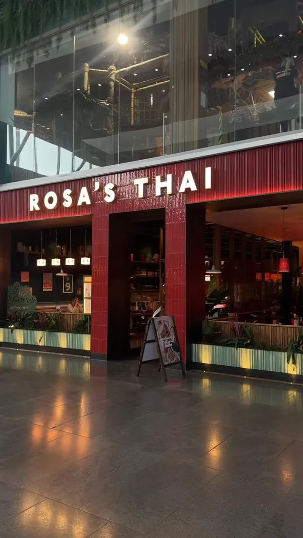 This video is a positive review of the restaurant Rosa's Thai, located in the Bluewater shopping centre. It begins with an exterior shot before moving inside to show a table laden with various dishes and drinks. The food items featured include prawn crackers, crispy prawn doughnuts, chicken satay, cashew chicken stir fry, and fried rice. The drinks highlighted are Thai Iced Tea, Thai Iced Coffee, and bubble tea. The creator provides a voiceover throughout, sharing her enthusiastic opinions on the meal, with a particular focus on how much she enjoyed the Thai Iced Tea. The video includes shots of the menu, close-ups of the food, and clips of the creator eating and drinking.