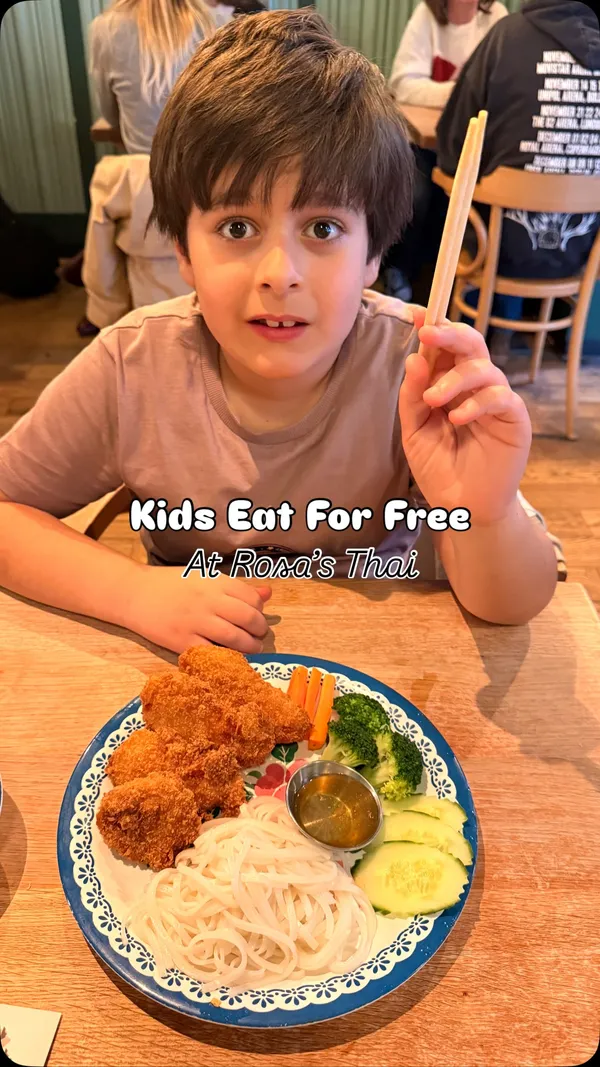The video promotes a 'kids eat free' offer at Rosa's Thai restaurant for the Easter period. It features two children enjoying different Thai dishes, including fried chicken with plain noodles and stir-fried noodles with chicken. An adult's meal, a Khao Soi noodle soup, is also showcased. The promotion is explained via text overlay and voiceover, stating that kids eat free when an adult orders a main meal. The video concludes by showing a child with a branded activity sheet and crayons provided by the restaurant.