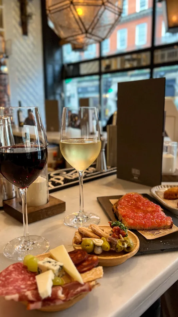 The video showcases a romantic date night at Ibérica Marylebone, a Spanish tapas bar in London. It features various tapas dishes, including a mixed gilda (anchovies, olives, peppers), croquetas (Serrano ham), toasted bread with tomato, and a selection of cured meats and cheeses.  The drinks include Cava, red wine, and white wine. The overall presentation is visually appealing and emphasizes the quality of the food and drinks.