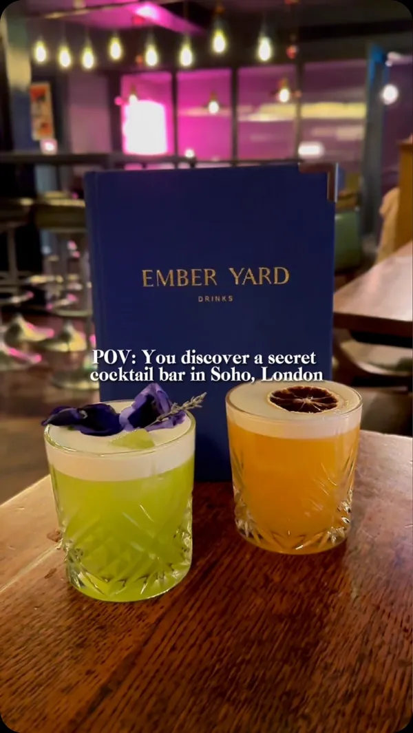 The video showcases Ember Yard, a cocktail bar in Soho, London. It features various cocktails, including a red cocktail with a sugared rim and an orange slice, an amber-colored old fashioned, and two other colorful cocktails. The setting is dimly lit, with a focus on the bar's ambiance and drinks. The video mainly highlights the bar's atmosphere and cocktails, with little to no food shown.