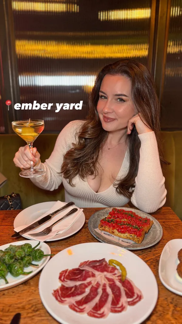 A female influencer visits Ember Yard restaurant in Soho, London, to try their tasting menu. The video showcases her experience, starting with cocktails (a martini and a margarita-style drink). She then enjoys a variety of tapas-style starters, including pan con tomate, cured meat, and ham croquettes. The main courses featured are large prawns in a red sauce, scallops served in their shells, and a paella-style dish with chicken and rice, accompanied by a side of tenderstem broccoli. For dessert, she tries a dark chocolate mousse and a Manchego cheesecake. The video highlights the food's presentation and the influencer's positive reactions, concluding with shots of the restaurant's downstairs bar area.