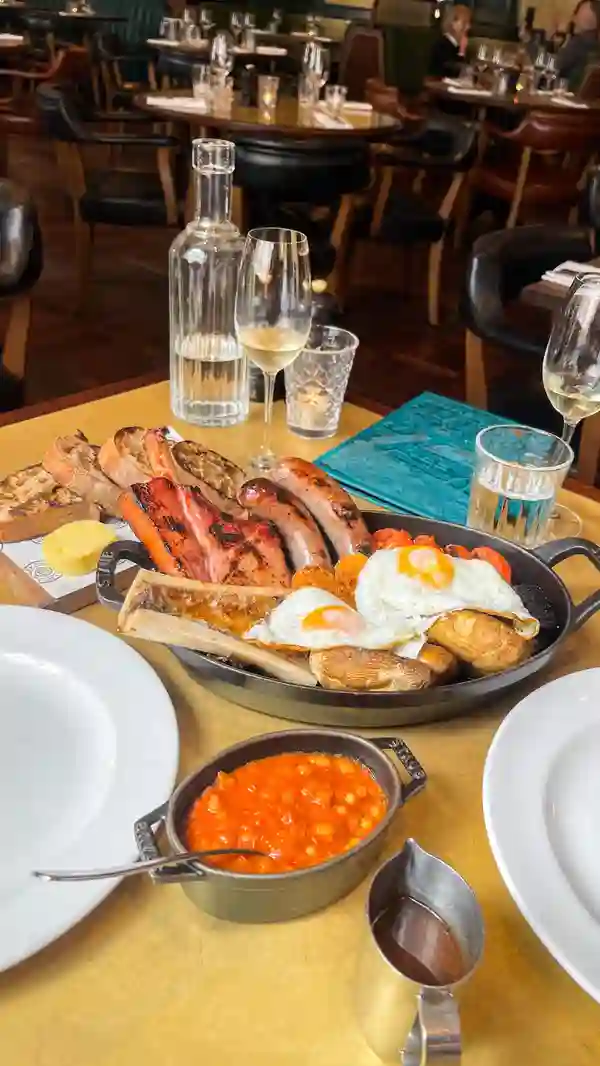 The video showcases a Saturday brunch sharer at Hawksmoor Liverpool. It features a variety of breakfast items, including a sugar-pit bacon chop, Victorian sausages, Moira black pudding, hash browns, grilled bone marrow, trotter baked beans, fried eggs, grilled mushrooms, roasted tomatoes, HP gravy, and unlimited sourdough toast. The food is presented in a rustic, hearty style, on both a large shared platter and individual plates. Two brunch cocktails are also highlighted: a Bloody Mary and a Blood Orange Mimosa.  The main focus is on the deliciousness of the food and drinks, highlighting the quality of the ingredients and cooking. The video encourages viewers to try the brunch.