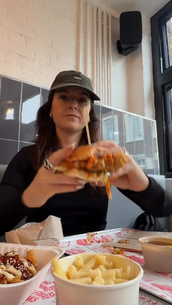 A review of the fried chicken restaurant 'Butchies'. The video showcases the creator eating a large meal, including a buffalo chicken burger, kimchi honey butter tenders, fries, and mac & cheese. It features close-up shots of the food, the restaurant's interior and exterior, and the menu. A voiceover provides a detailed review of the food and tells the story of the brand's origin as a street food stall.