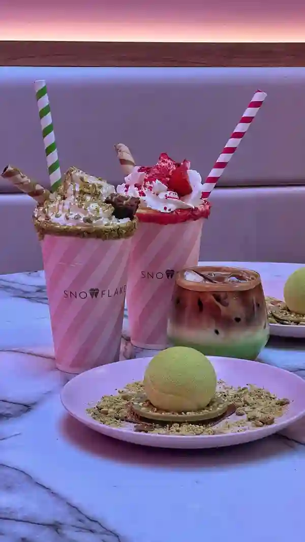 The video showcases Snowflake Gelato's new summer menu, featuring a Wimbledon-inspired gelato tennis ball (strawberry and cream with pistachio base), and milkshake/sundae hybrids.  The setting is the Snowflake Gelato cafe, with a modern and brightly lit interior. The gelato is presented on a pink plate, and the milkshakes in branded cups. Dietary information is not explicitly provided. The main focus is a product showcase, highlighting the visual appeal and variety of the menu items.