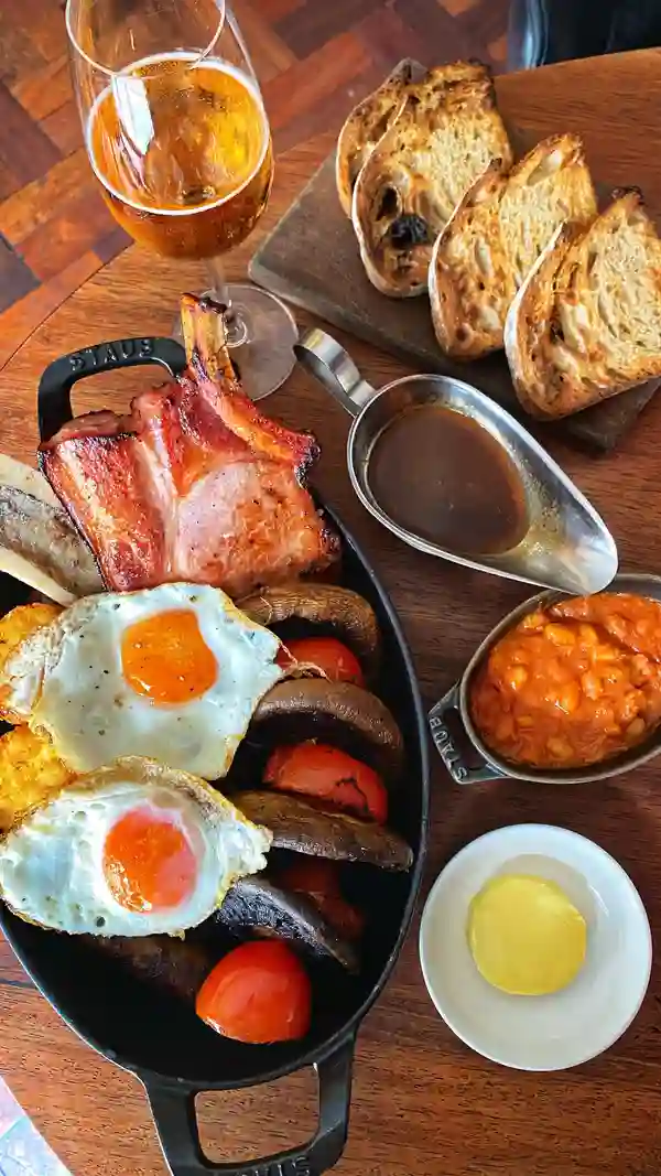 The video showcases a luxurious English breakfast feast at Hawksmoor Air Street restaurant in London. The setting is a high-end restaurant with a modern and stylish ambiance. The food items include a smoked bacon chop, sausage, black pudding, hash browns, grilled bone marrow, trotter baked beans, fried eggs, grilled mushrooms, roast tomatoes, HP gravy, and sourdough bread with butter. The presentation is visually appealing, with a focus on the rich colors and textures of the food. The video also highlights the restaurant's cocktails. The main focus is a meal showcase.