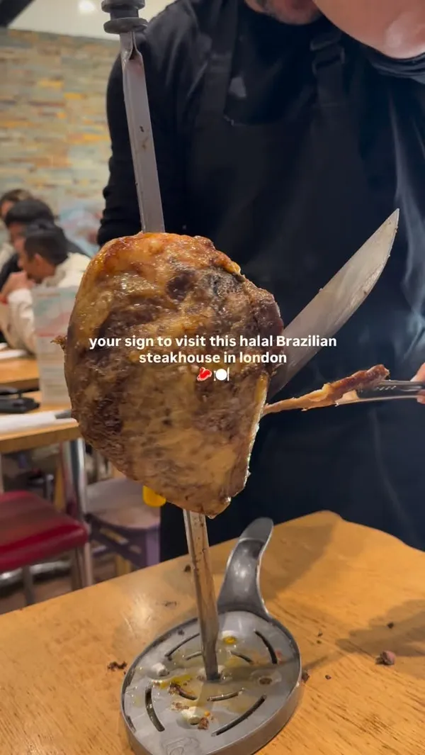 The video showcases a dining experience at a halal Brazilian steakhouse in London. It opens with a server carving a large piece of roasted meat from a skewer at the table. Subsequent shots display two full plates of food, featuring sliced steak, fries, and a variety of salads from a buffet. The video also shows two cocktails and concludes with a shot of a chocolate cake dessert with ice cream.