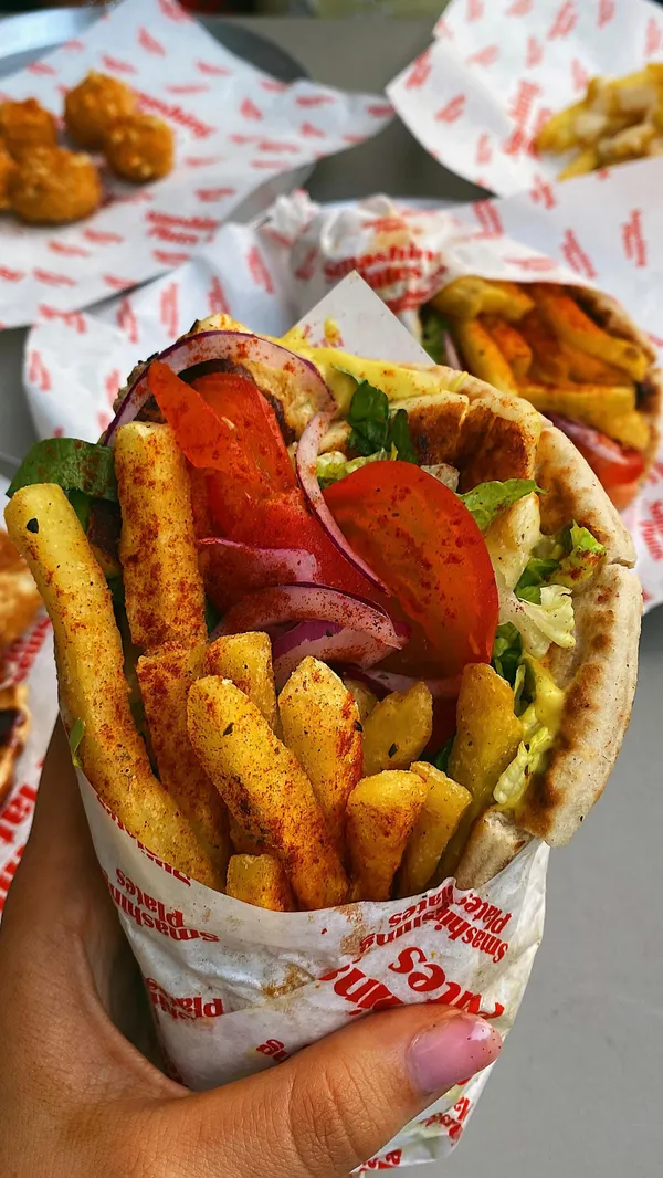 The video showcases Smashing Plates, a Greek street food vendor in London. It highlights various menu items, including souvlaki wraps with halloumi and fries, pitanuts (pitta donuts with chocolate sauce), and a Greek salad. The food is presented in visually appealing ways, emphasizing its freshness and tastiness.  The video also showcases the self-service kiosks and mentions that veggie/vegan options are available. The primary focus is a meal showcase, with the influencer enthusiastically endorsing the food.