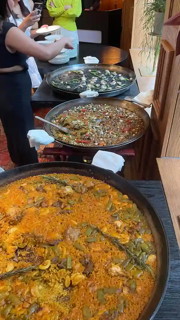 The video showcases a luxurious dining experience at a restaurant called Arros QD. It features various food and drink items, including cocktails served in rose-shaped glasses, champagne, tapas-style appetizers (tuna cones and a yellow foam dish), fried shrimp, paella (three varieties: black, mixed seafood, and a lighter yellow variation), and a chocolate dessert. The presentation is sophisticated and visually appealing, with high-quality ingredients and elegant plating.  The venue is modern and stylish.