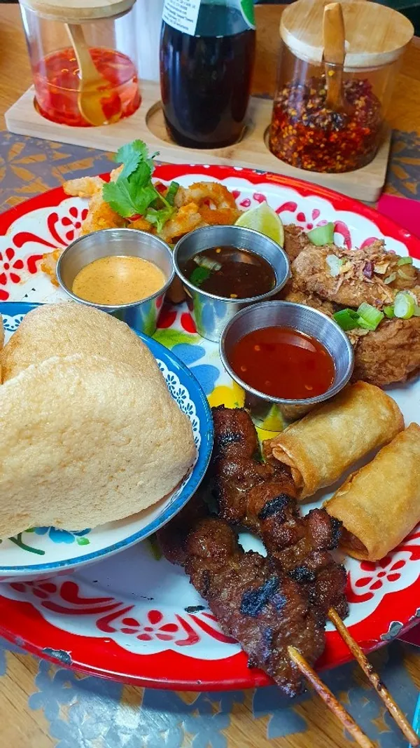 The video showcases Rosa's Thai restaurant, beginning with exterior shots and views of the Albert Dock. It transitions to interior views, showing the decor, staff, and customers. The focus shifts to the food and drinks, featuring two bubble teas, a starter platter with items like skewers, spring rolls, prawn crackers, fried prawns, and dips, a plate of Pad Thai, and desserts including a Somtum brownie with ice cream and Thai churros. The influencer is shown holding the starter platter and eating the Pad Thai.