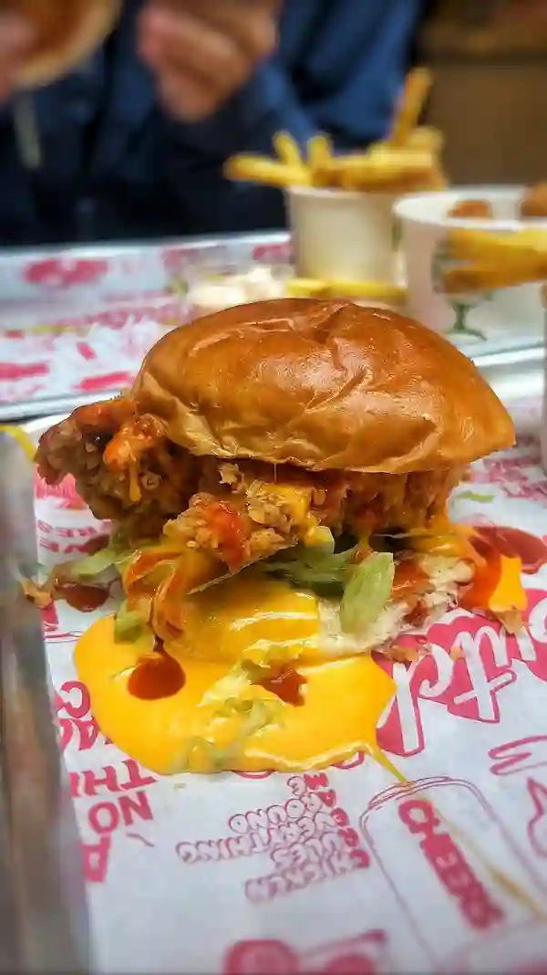 The video showcases various fried buttermilk chicken dishes from Butchies, a restaurant with multiple London locations. It features close-ups of burgers (the 'OG' Burger and Cheesy Rider Burger), chicken tenders, popcorn chicken, and fries. The presentation emphasizes the golden-brown, crispy texture of the fried chicken and the generous amounts of cheese and sauce. No dietary information is explicitly provided.