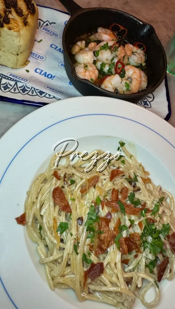 A promotional video for the new Prezzo Italian restaurant on George Street in Edinburgh. The video showcases the restaurant's spacious, modern interior with an open kitchen and bar area. It features a variety of dishes, including a crispy chicken Caesar salad, a large calzone with a side salad, a burger with fries, spaghetti carbonara, oven-baked king prawns with bread, and desserts like doughnut balls with chocolate dip and a chocolate cookie dough skillet with ice cream. The video highlights family-friendly aspects and a special 'rock, paper, scissors' promotion for a 2-for-1 dessert.