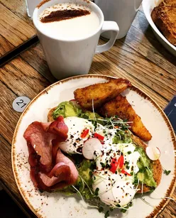 Smashed avocado toast with poached eggs, bacon, hash browns, chipotle, chili, and oat chai latte at BTP Cafes brunch.