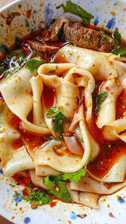 Biang biang noodles served in Lanzhou style beef broth with Sichuan chili oil and herbs, ready to slurp.