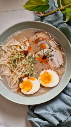 Bowl of rich tonkotsu ramen topped with chashu pork, seaweed, sesame, chili oil, and a soy tea egg.