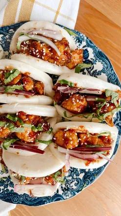 Sticky chicken bao buns with honey chili sauce, raw red onion, and sesame oil, perfect for impressing guests.