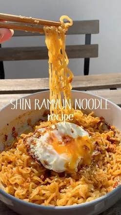 Bowl of shin ramyun noodles topped with a fried egg, sesame seeds, and crispy onions, ready to eat.