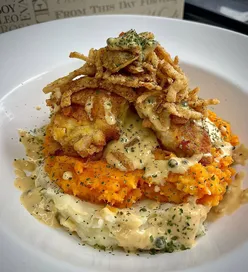 Homemade southern fried chicken stack with grilled onions, peppercorn sauce, mash potatoes, carrot, and parsnip.