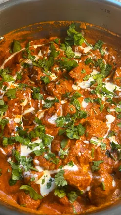 Butter chicken with creamy sauce and spices, garnished with coriander, served with garlic naan; cooked in ProCook dish.