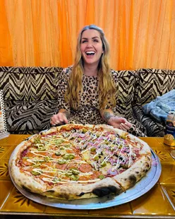 Happy couple enjoying 20-inch vegan pizza at Yeastie Boys Pizza Club, Brighton; half SGT Pepper, half Shroominโ with olives.