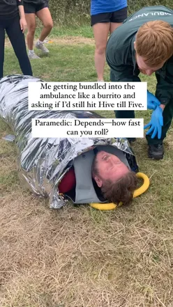Person wrapped like a burrito in an ambulance, humorously asking paramedic about reaching Hive till Five. #BurritoLife #Foodie