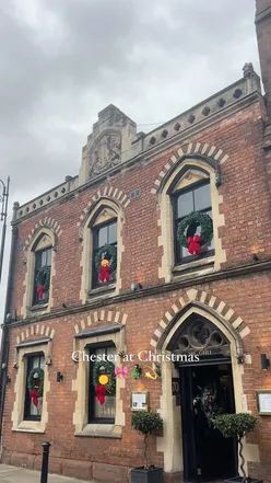 Festive Chester scene with Eastgate clock, flickering Xmas lights, Dinky Donuts aroma, and shopfronts adorned with wreaths.