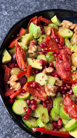 Colorful winter salad with pomegranate, olives, cucumbers, cherry tomatoes, avocado, walnuts, and olive oil dressing.