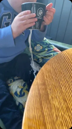 Toddler playfully disrupts food video shoot, giggling with spilled juice and scattered snacks on kitchen floor.