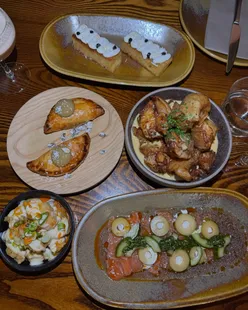 Diverse dishes at Exhibition MCR: brioche toast, tempura crab, salmon sashimi, herb-fed chicken, crispy potatoes, short-rib empanadas, fried chorizo, Basque cheesecake.