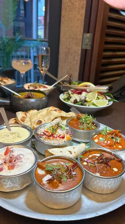 Indian restaurant meal with lamb chops, ribs, and bottomless thali featuring curries, rice, naan, and mango lassi.