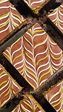 Fudgy pistachio kunafa chocolate brownies topped with melted chocolate and pistachio cream, showcasing a delicious dessert.