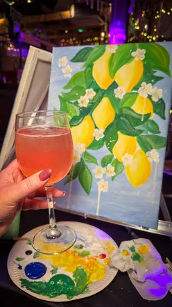 Person holding a cocktail and paintbrush, enjoying a Paint and Sip night in Cardiff with friends.