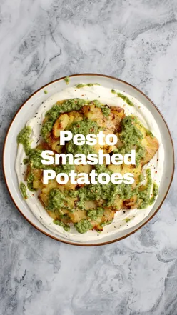 Crispy smashed potatoes topped with homemade pesto and lemony whipped ricotta on a plate.
