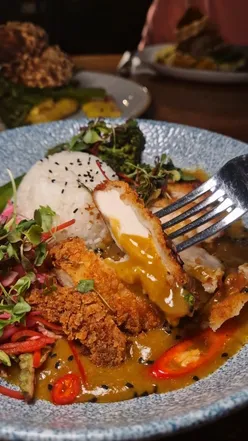Cozy pub interior featuring a delicious katsu curry with sauce and pickled vegetables, perfect comfort food.