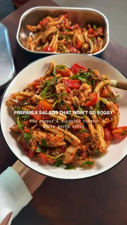 Colorful red pepper and sundried tomato pesto pasta salad with chicken, tomatoes, and rocket for meal prep.