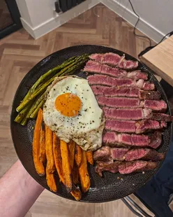 Thick cut dry-aged sirloin with sweet potato fries, garlic roasted asparagus, and a golden yolked egg, home-cooked meal.
