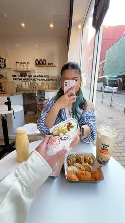 Two friends enjoying bubble tea and dessert in Birmingham's Chinatown, celebrating with cheers.