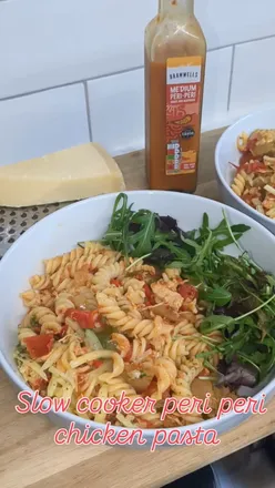 Slow cooker peri peri chicken pasta with veggies, topped with cheese, served with rocket and parmesan.