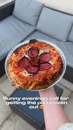 Freshly baked pepperoni pizza from a Gino pizza oven, enjoyed in a sunny garden setting.