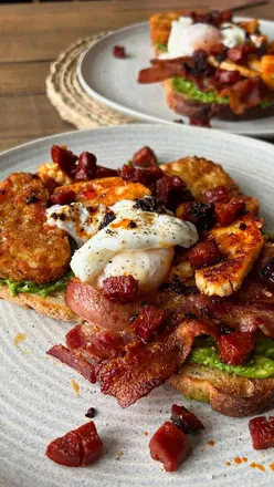 Toasted sourdough topped with smashed avocado, crispy bacon, chorizo, hash browns, honey-drizzled halloumi, and poached egg.