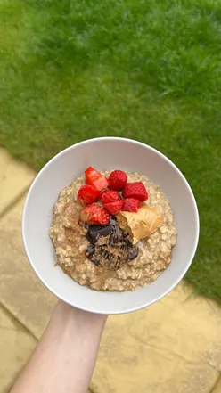 Vegan vanilla protein porridge topped with dark chocolate, strawberries, honey, and peanut butter.