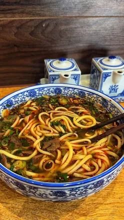 A massive bowl of Lanzhou hand-pulled beef noodles from Kung Fu Noodle in Birmingham, showcasing vibrant flavors.