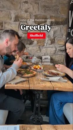 Family enjoying Greek and Italian dishes at Greetaly cafΓ© in Sheffield, featuring moussaka, pizza, and tiramisu.