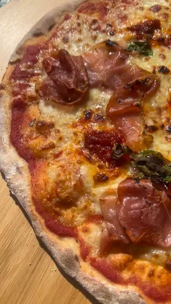 Homemade stone-baked pizza cooking in an Ooni pizza oven under the summer sun in a garden setting.