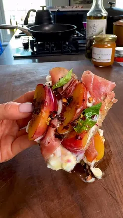 Hot honey grilled peach and cottage cheese toast topped with prosciutto, red onion, and fresh basil.