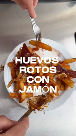 Plate of huevos rotos with jamón, fried eggs, onions, and potatoes, showcasing Andalusian cuisine.