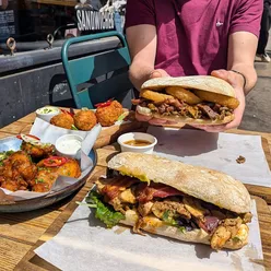 Juicy steak sandwich with onion rings and peppercorn sauce at Social Board, Kemptown, Brighton; vibrant street scene.