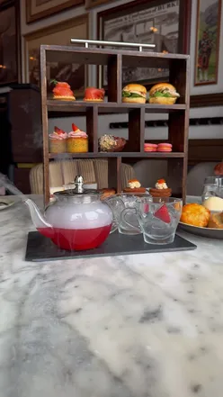 Afternoon tea at Twenty Princes Street, Edinburgh, featuring a smoky gin cocktail in a glass teapot, salmon tart, and pistachio financier.