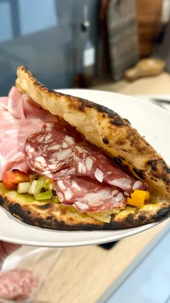 Mortadella and salami panuozzo with pesto, sun-dried tomatoes, Parmesan, mozzarella, and garlicky leeks, inspired by Italian sandwiches.